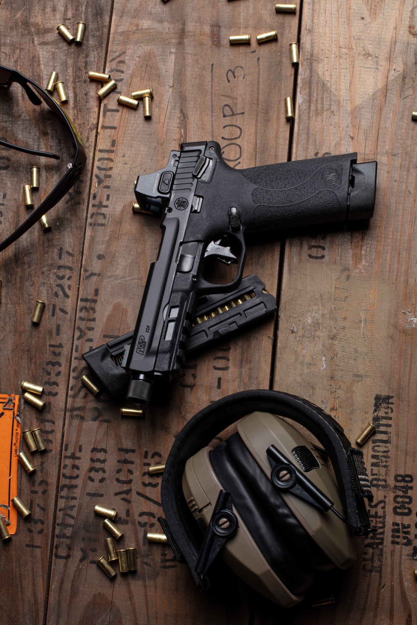 Pistole auf Holzuntergrund mit Patronen und Gehörschutz.
